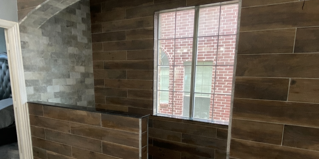 Custom master bathroom remodel in Allen TX featuring wood-look tile walls, arched shower entry, and pebble stone shower floor by Bath Masters of Collin County